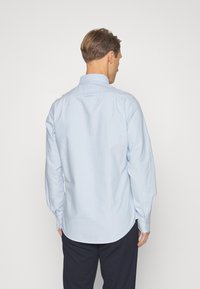 Camicia a maniche lunghe azzurro chiaro in cotone. Presenta un colletto a camicia, una piega sul retro e polsini con bottone, con una texture liscia.