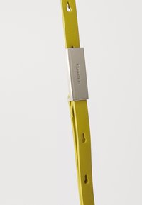 Cinturino per orologio in silicone giallo con vestibilità regolabile, dotato di una fibbia metallica argento impreziosita dalla scritta "Calvin Klein". Texture liscia, design minimal.