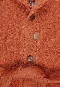 Cotton bathrobe in burnt orange with a textured, terry fabric. Features wooden buttons and a fabric tie belt. Small brand label visible.