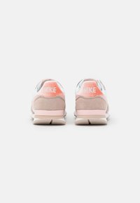 Baskets Nike avec une partie supérieure en mesh blanc, des accents en suède rose clair et beige, un logo proéminent sur le talon et un col rembourré.