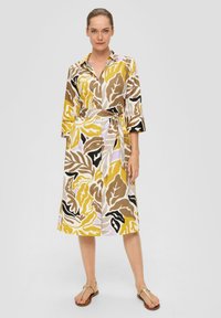 Robe collerette avec un motif de feuilles audacieux, accentuée de jaune, marron et noir. Dotée d'une taille ceinturée, de manches trois-quarts et d'une coupe jusqu'aux genoux.