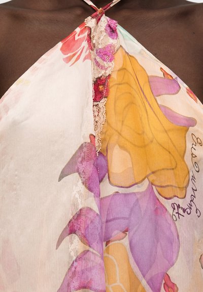 Διάφανο τοπ με halter, με μεγάλο κίτρινο και μοβ λουλουδάτο σχέδιο και ροζ δαντέλα σε σκουρόχρωμο δέρμα.