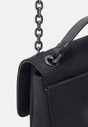 Gros plan d’un sac à main noir texturé avec une poignée en cuir et une bandoulière chaîne en métal brillant attachée par une quincaillerie ronde en métal gravée.