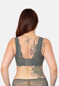 Grüner Spitzen-BH mit breiten Trägern und zartem Blumenmuster, mit einem Haken- und Ösenverschluss auf der Rückseite, der filigrane Texturen zeigt.