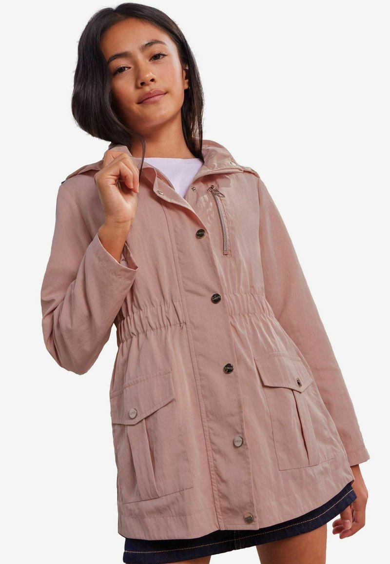 Chaqueta exterior ligera de color rosa claro, con cordón en la cintura, bolsillos frontales y capucha. Presenta botones a presión y una textura suave.