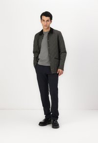 Quilted, mørkegrøn jakke med store knapper, brun krave, grå t-shirt, marineblå ternede bukser og sorte sko.