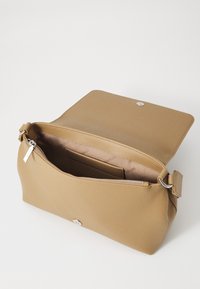 Beżowa torebka na ramię z syntetycznej skóry, wyposażona w główną przegrodę na zamek błyskawiczny, magnetyczne zapięcie na klapę oraz gładką fakturę. Wewnątrz znajduje się kieszonka.