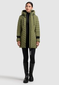 Parka imbottita verde oliva con cappuccio, chiusura con zip e trapuntatura diagonale. Presenta polsini neri e un'etichetta con logo sul cursore della zip.