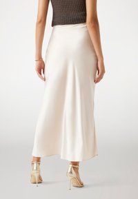 Satin, krämfärgad kjol med en flödande design. En figursydd midja sträcker sig till knäna. Innehåller guldhögklackade öppna skor.