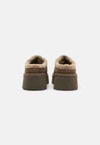 Scarpe slip-on in suede marrone con una morbida fodera beige, retro arrotondato, suola spessa marrone e logo del marchio delicatamente impresso sul tallone.