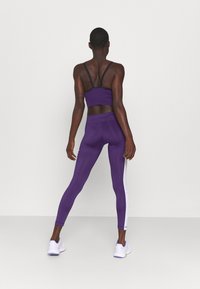 Lila sport-bh och leggings med svarta detaljer; leggings har vita sidostripes. Materialet verkar elastiskt och tajt.