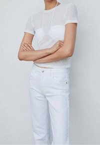 Top blanco de manga corta con textura acanalada y diseño ajustado, combinado con unos jeans blancos de cintura alta que cuentan con un botón frontal y detalles de bolsillos.