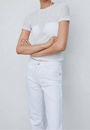 Top blanco de manga corta con textura acanalada y diseño ajustado, combinado con unos jeans blancos de cintura alta que cuentan con un botón frontal y detalles de bolsillos.