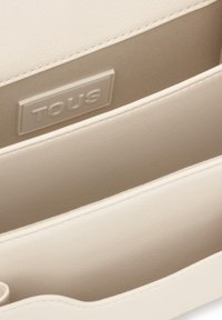 Portefeuille en similicuir beige avec une surface texturée, comprenant deux compartiments et un logo "TOUS" embossé à l'intérieur.