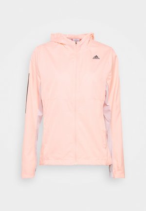 Veste coupe-vent rose clair avec fermeture éclair à l'avant, capuche ajustable et accents noirs sur les manches. Fabriquée en matériau lisse et léger.