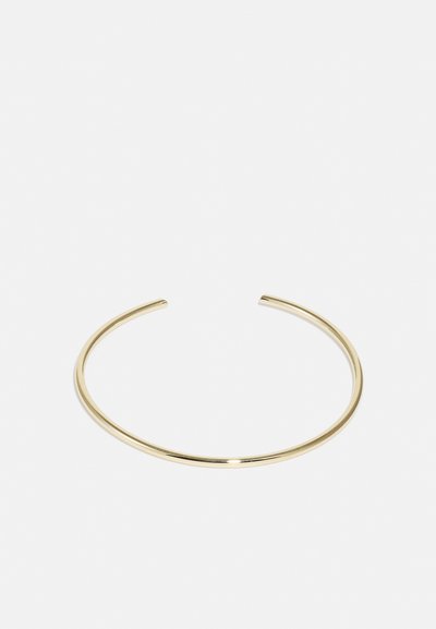 Bratara din metal de culoare aurie, cu suprafață netedă, formă rotundă, design deschis cu extremități conice. Apariție simplă, minimală.