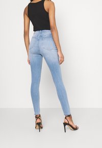 Světlé modré skinny džíny s vysokým pasem, se standardními pěti kapsami a prošíváním, kombinované s černými sandály na páscích.