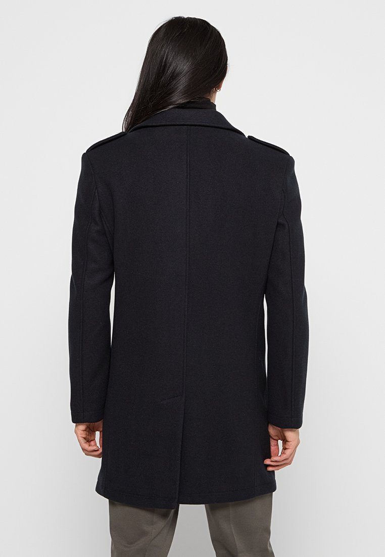 Cappotto in lana nera con colletto strutturato, maniche lunghe, spacco sul retro e due tasche laterali. Texture liscia e vestibilità sartoriale.