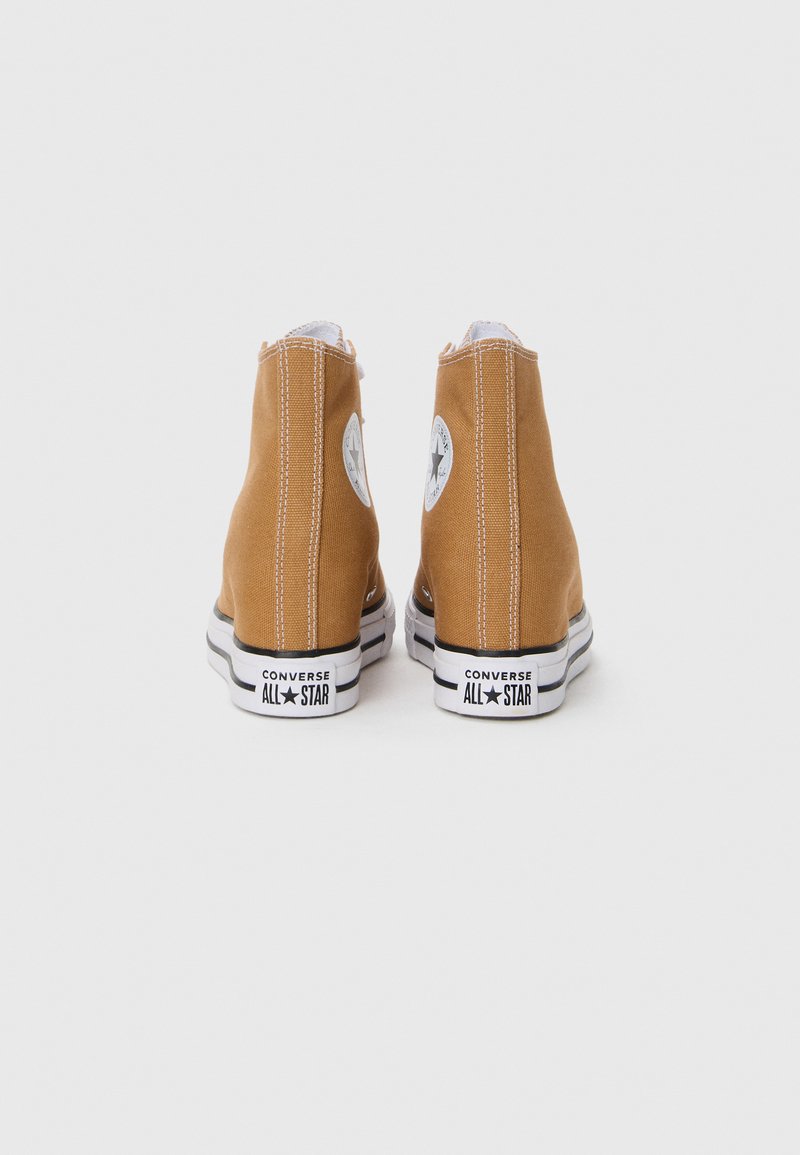 Beige canvas högstövlar med vit gummisula, svarta accenter och runda logotyper på sidorna. Har dubbla sömmar för ökad hållbarhet.