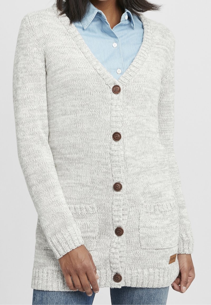 Ljusgrå cardigan gjord av kraftig stickad material. Har V-ringning, träknappar, två framfickor och ribbade manschetter.