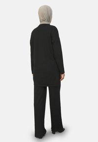 Zwart langwaardig top met een ontspannen pasvorm en een hoog- laag zoom, gecombineerd met bijpassende wijde broek. Gladde stof, eenvoudig ontwerp, geen patronen.
