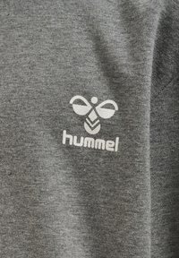 Szara koszulka z miękkiego materiału z białym logotypem, który przedstawia stylizowaną pszczołę oraz nazwę marki "hummel" poniżej.
