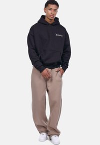 Black cotton hoodie with front pocket and white "Dropsite" text, paired with beige sweatpants and white sneakers. Simple, relaxed fit.