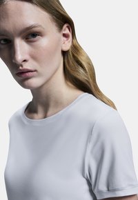 Ljusgrå t-shirt med kort ärm och rund halsringning i slät, texturerad tyg. Närbild som lyfter fram halsringningen och axelpartiet.