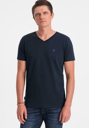 Camiseta V de color azul marino hecha de una mezcla de algodón, con mangas cortas y un pequeño logo en el pecho. Se lleva con jeans azules.