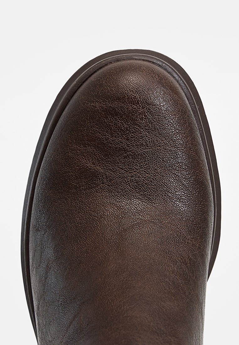Scarpa in pelle marrone con punta arrotondata, finitura testurizzata e suola in gomma resistente. Design minimalista, senza hardware o motivi visibili.