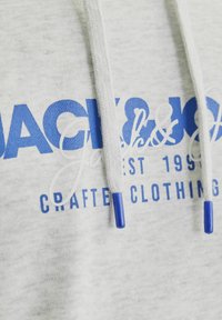 Sudadera de color gris claro con texto impreso en azul y blanco, que incluye "JACK & JONES CRAFTED CLOTHING", con cordones blancos y puntas azules.