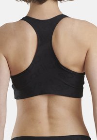 Svart sportbh med racerback-design. Tillverkad av texturerat tyg med en subtil logotypmönster. Släta kanter och figurnära siluett.