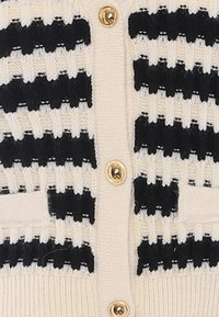 Cardigan lavorato a maglia con base crema e motivo a righe nere, dotato di bottoni dorati e tasche frontali testurizzate.