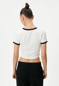 Camiseta corta blanca con canalé y borde negro en el escote y las mangas. Presenta una silueta ajustada y una textura suave.
