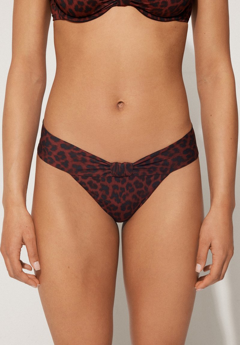 Bikiny s leopardím potiskem v hnědé a černé barvě, s uzlovým designem v přední části. Tkanina vypadá hladce a pružně, s nízkým střihem.
