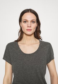 Pelēka īsām piedurknēm t-kreklu ar apaļu kakla izgriezumu, izgatavots no mīksta, teksturēta auduma. Krekls ir brīvs un tam ir minimālas detaļas.