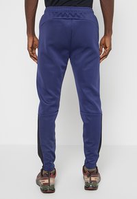 Granatowe spodnie sportowe z elastycznym paskiem w talii i czarnymi bocznymi panelami, charakteryzujące się gładką fakturą i zwężanymi nogawkami.