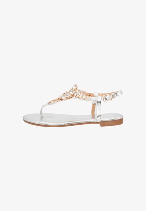 Silberne flache Sandale mit Zehensteg, durchsichtiger Überlagerung und einem verzierten Riemen mit juwelähnlichen Akzenten. Die Sohle ist hellbraun.