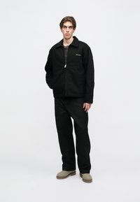 Μαύρο φούτερ με φερμουάρ και γιακά, συνδυασμένο με μαύρες χαλαρές παντελόνες και ανοιχτού γκρι μποτάκια. Καθαρός, μινιμαλιστικός σχεδιασμός.