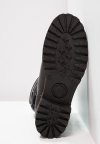 Black rubber boot sole with deep grooves for traction, featuring a circular logo and size marking. Textured for enhanced grip and durability.