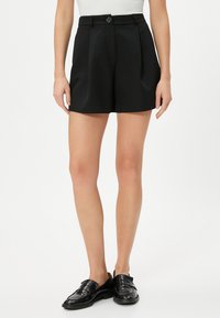 Zwarte op maat gemaakte shorts van gladde stof, met een knoopsluiting, plooien aan de voorkant en zijzakken. Geschikt voor casual draag.