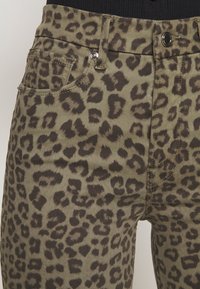 Pantalon vert olive avec imprimé léopard marron foncé, doté de poches avant, passants pour ceinture et d'une fermeture à bouton métallique.