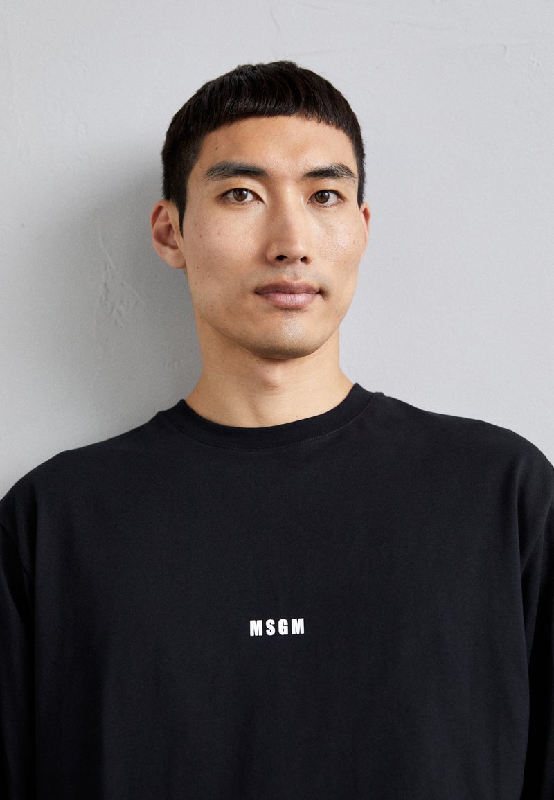 Black long-sleeve t-shirt made of cotton. Features a round neckline and a white "MSGM" logo on the chest. Smooth texture, casual fit.