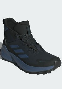 Bota de senderismo en negro y azul marino con parte superior texturizada, material impermeable, suela texturizada y tres franjas horizontales en azul marino. Marca Gore-Tex visible.