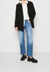 Černý pruhovaný blazer přes bílou košili, doplněný o světle modré rovné džíny a černé robustní loafery. Hladké textury, jednoduchý design.