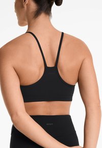 Zwarte sportbeha met dunne bandjes, gladde textuur en logo-detail op de achterkant. Heeft een racerback-ontwerp voor extra ondersteuning.