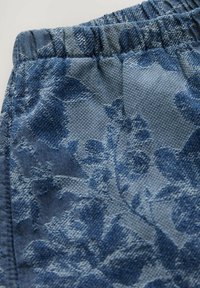 Modrý vzorovaný textil s textúrovaným kvetinovým dizajnom a elastickým pásom. Materiál vyzerá tkaný s jemným leskom.
