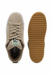 Beige suede sneakers with white rubber sole, textured gum outsole, round toe, and flat laces. Features a green and white Puma logo label.