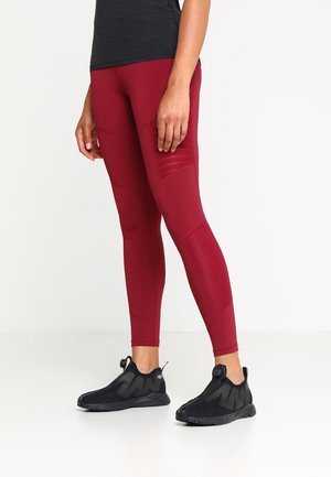Leggings sportivi rossi con pannelli texture, abbinati a scarpe nere slip-on con tomaia in rete e punta rotonda.