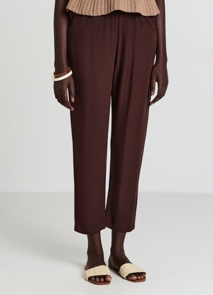 Pantaloni marroni a gamba larga con una texture liscia e vita elasticizzata, abbinati a un sandalo a fascia color crema. Nessun dettaglio aggiuntivo riportato.